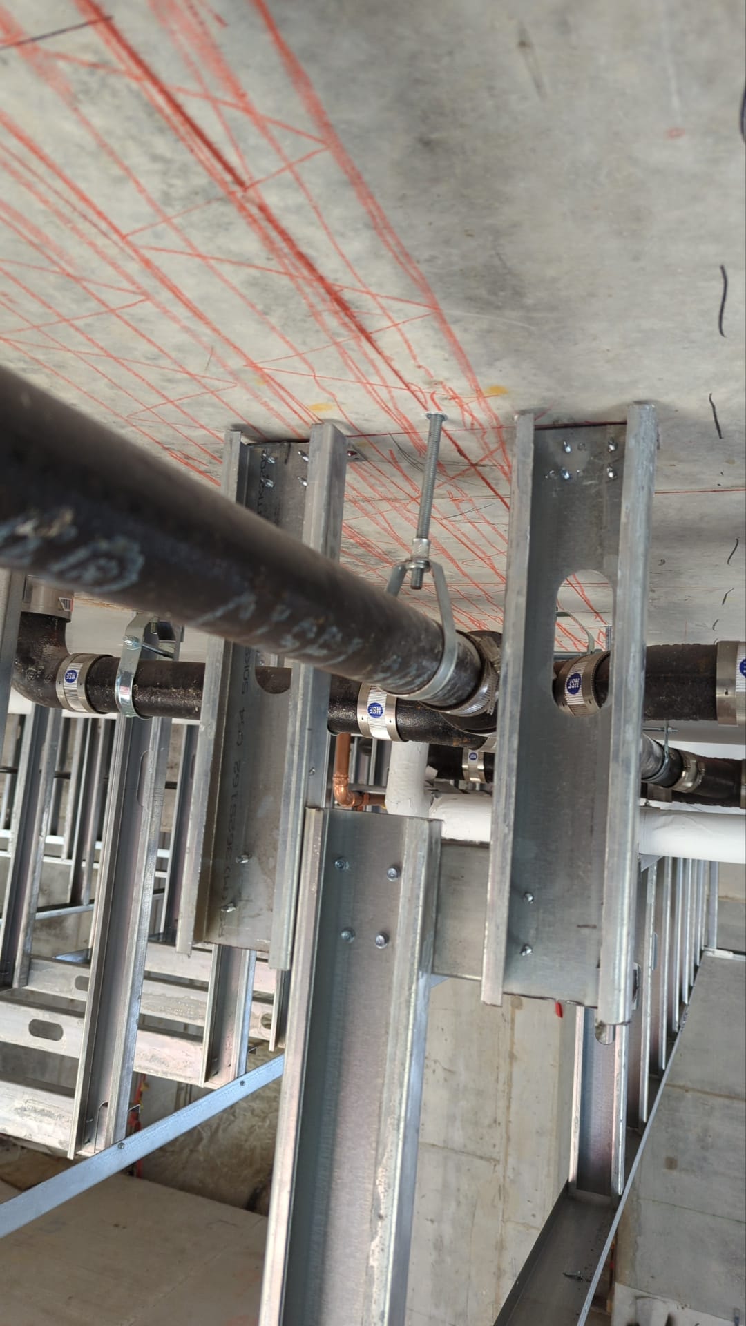 Steel stud framing with pipe penetrations and layout marks on concrete ceiling