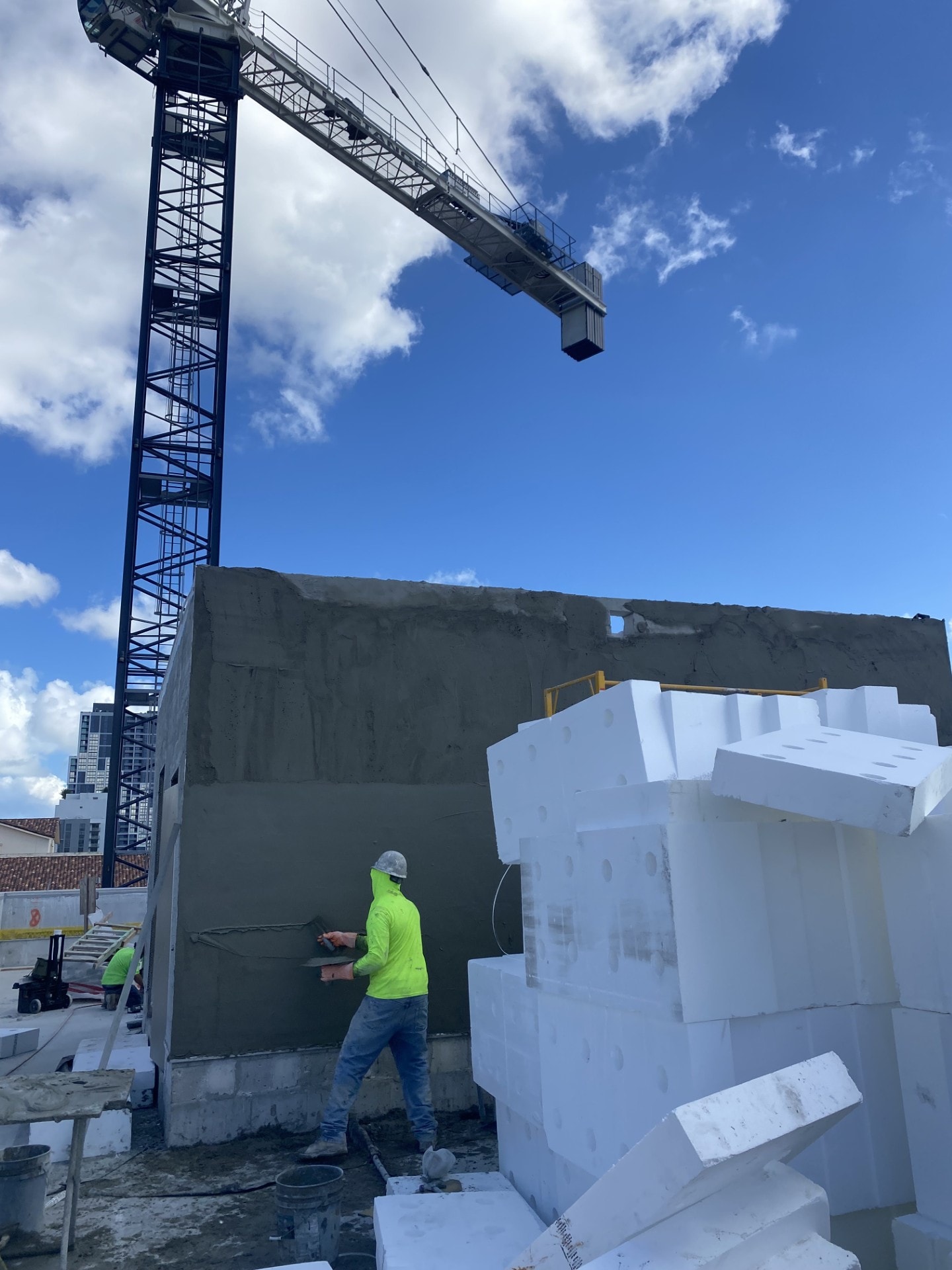 Worker applying stucco with crane in background — Miami highrise site