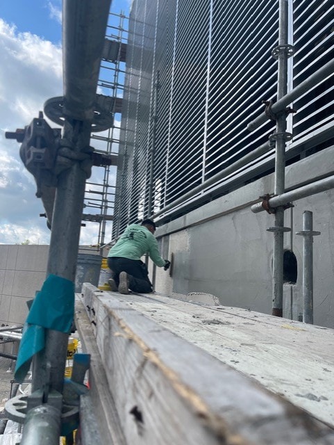 Worker on scaffolding performing close-up stucco repair